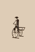 Recycled-metal Bicycle Planter with a cyclist figure showing its empty rear pot holder against beige.