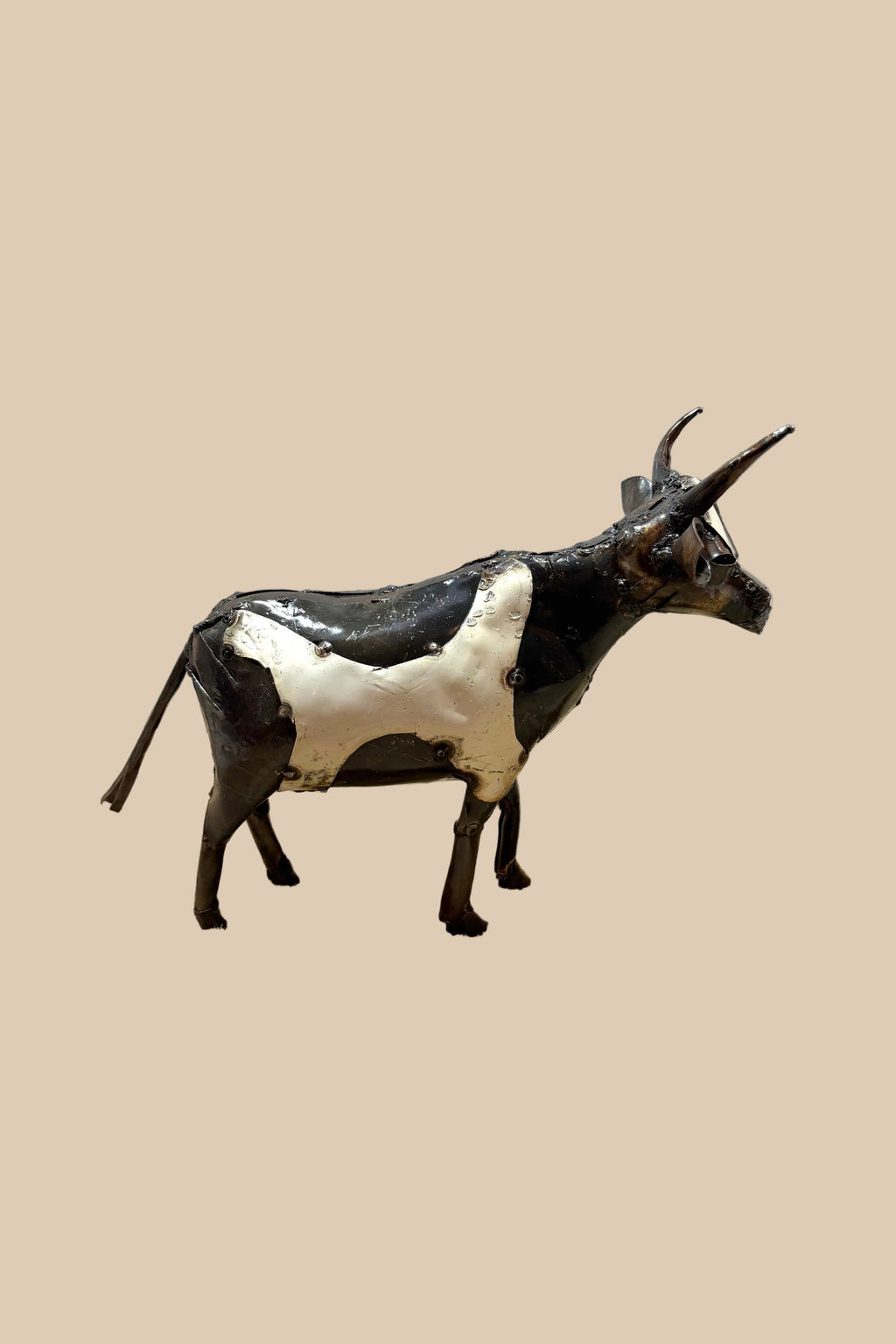 Black-and-white recycled-metal cow with long curved horns, in side profile.