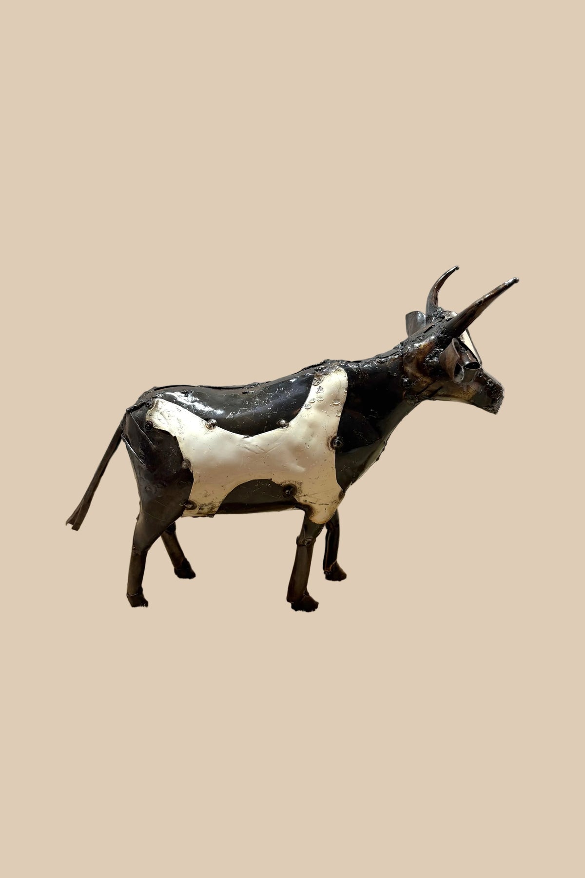 Black-and-white recycled-metal cow with long curved horns, in side profile.
