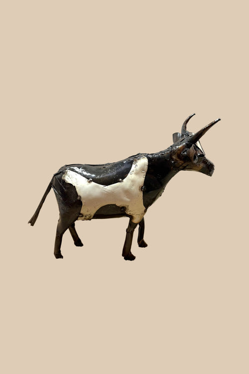 Black-and-white recycled-metal cow with long curved horns, in side profile.