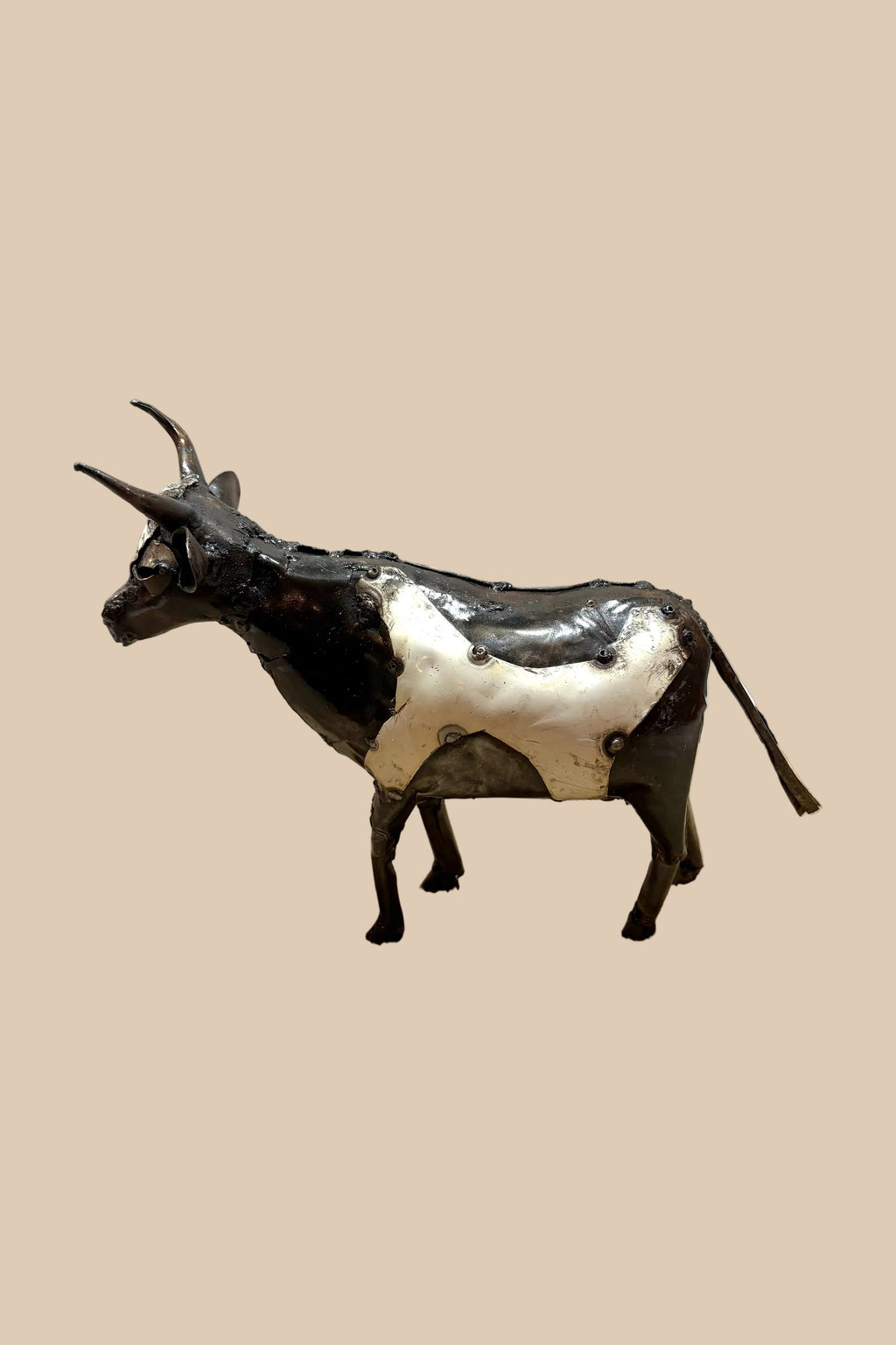 Black-and-white recycled-metal cow with long curved horns, viewed from the opposite side.