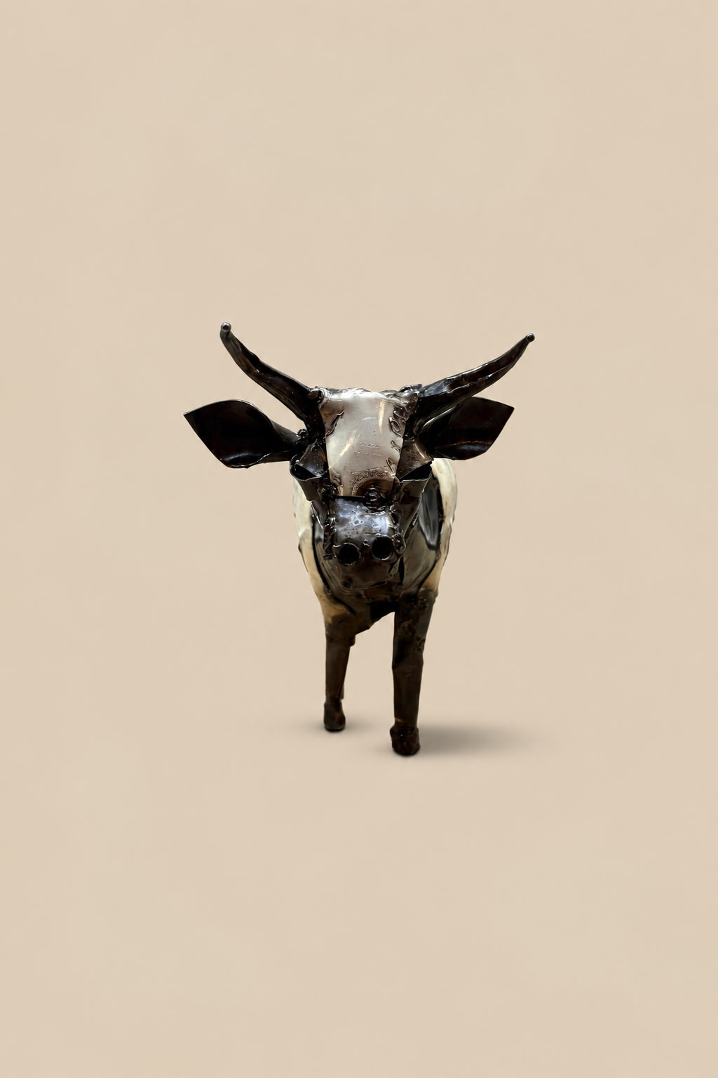 Black-and-white recycled-metal cow with long curved horns, viewed from the front.