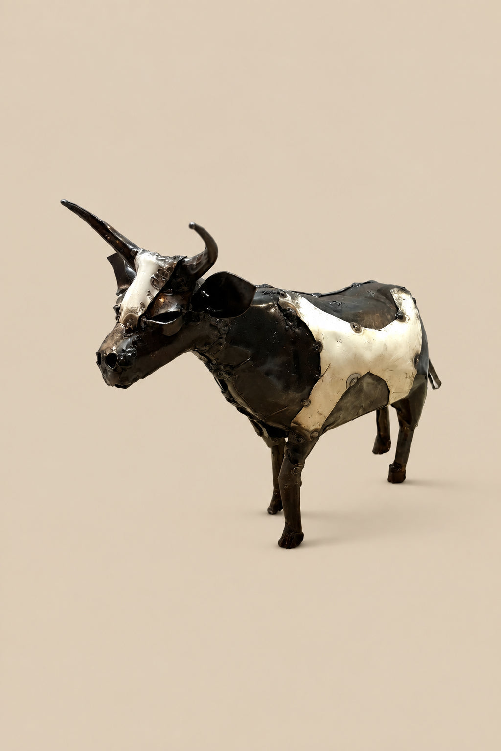 Black-and-white recycled-metal cow with long curved horns, viewed from the front at an angle.