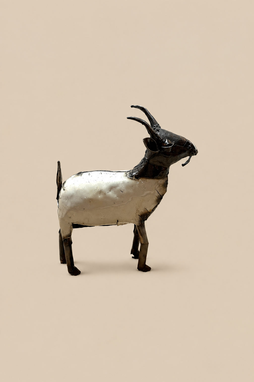 Cream-and-black recycled-metal goat with curved horns, viewed from the opposite side.