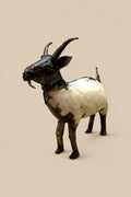 Cream-and-black recycled-metal goat with curved horns, viewed from the front at an angle.