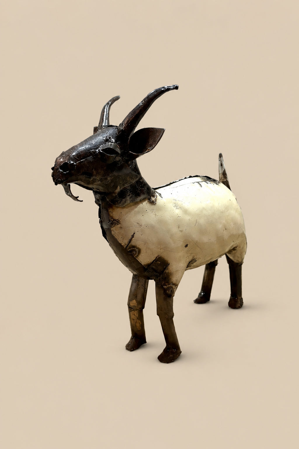 Cream-and-black recycled-metal goat with curved horns, viewed from the front at an angle.