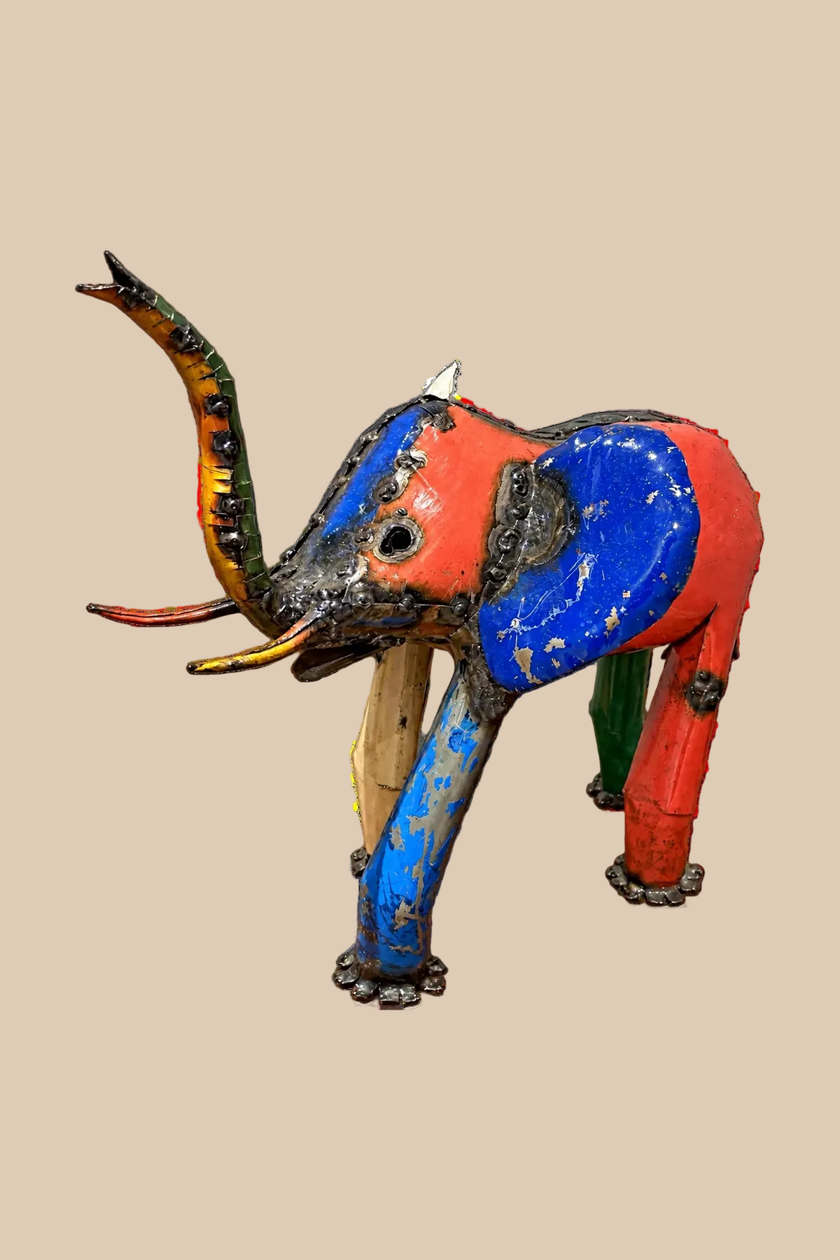 Medium Elephant sculpture in colourful reclaimed metal with a raised trunk, with red and blue panels, side view.