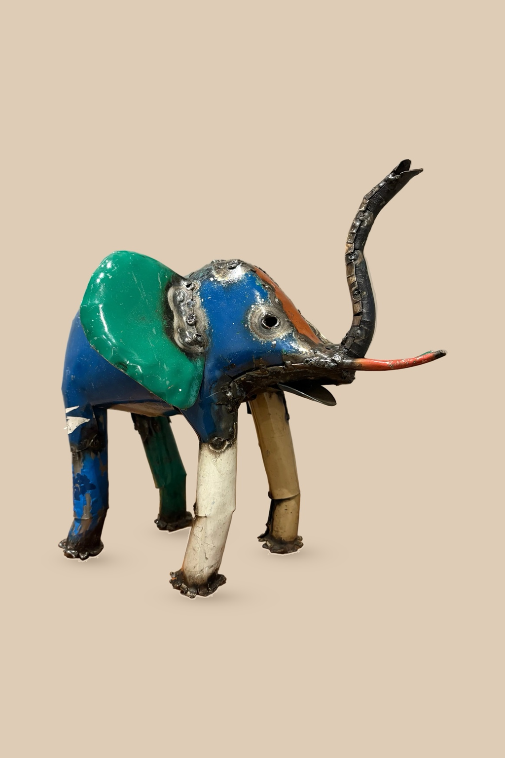Medium Elephant sculpture in colourful reclaimed metal with a raised trunk, with green and blue panels, side view.