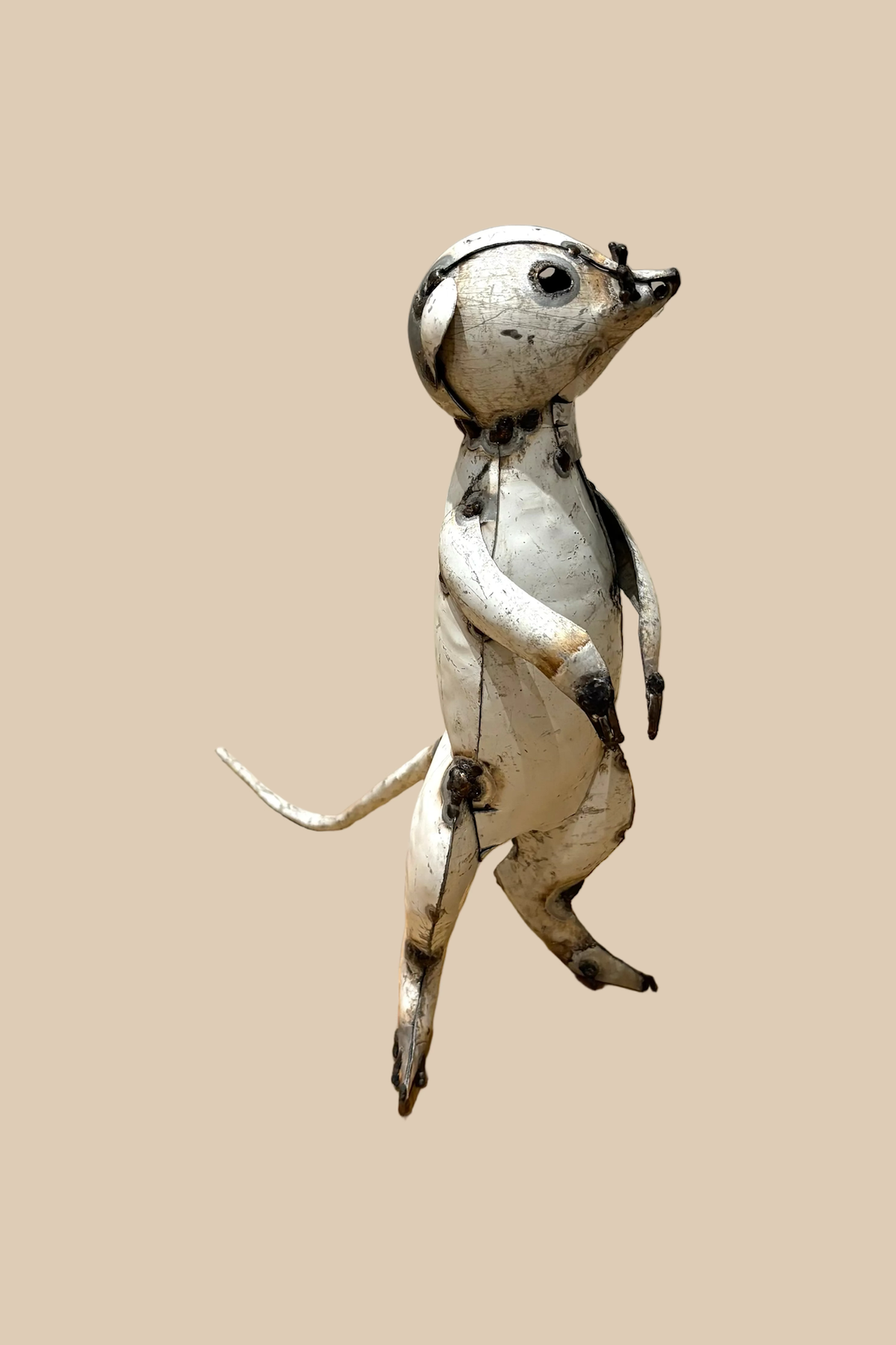 Pale recycled-metal meerkat standing upright with its forepaws raised, viewed from the opposite front angle.