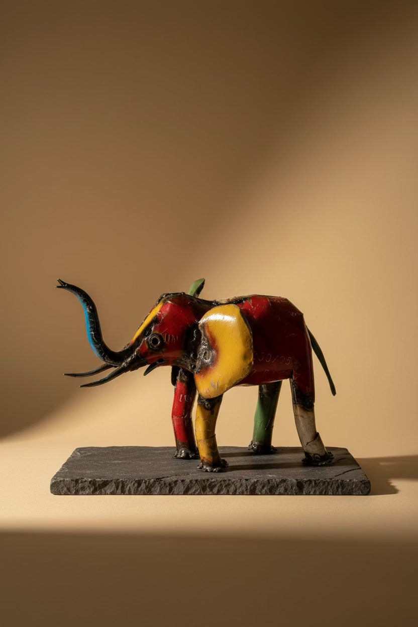 Small recycled metal elephant sculpture on dark stone in warm studio light